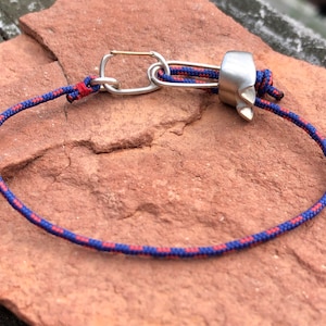 May include: A blue and red rope with a silver carabiner and a silver metal climbing device.