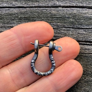 May include: A silver-toned metal earring with a U-shaped design and a small pin. The earring has the words "The U.S.A." engraved on it.