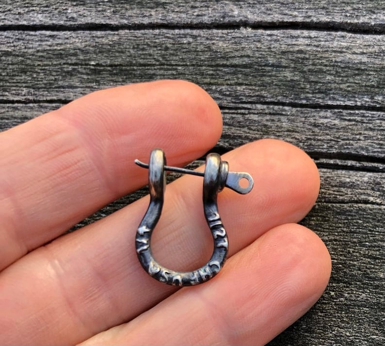 May include: A silver-toned metal earring with a U-shaped design and a small pin. The earring has the words "The U.S.A." engraved on it.