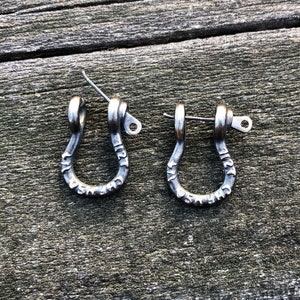 Könnte beinhalten: Ein Paar silberne Ohrringe in U-Form mit einer kleinen Schlaufe oben. Die Ohrringe sind mit den Worten "Made in USA" graviert.