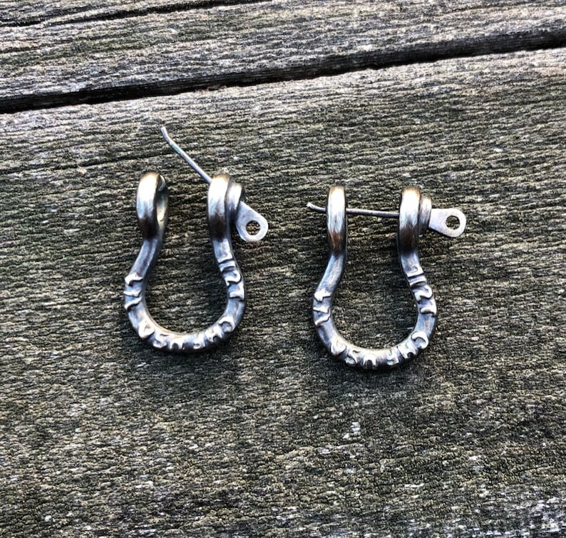 May include: A pair of silver metal earrings shaped like a U with a small loop at the top. The earrings are engraved with the words "Made in USA".