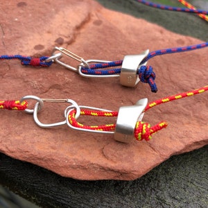 May include: Two silver climbing carabiners with red and yellow ropes attached. The carabiners are on a brown rock surface.