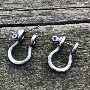 May include: A pair of silver-toned metal earrings shaped like a U-shaped hook. The earrings have a simple, minimalist design.