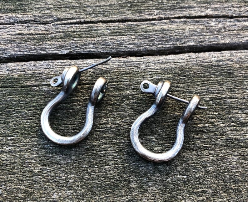 May include: A pair of silver-toned metal earrings shaped like a U-shaped hook. The earrings have a simple, minimalist design.