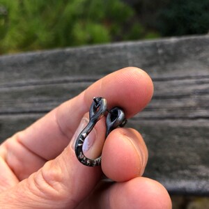 May include: A silver hoop earring with a textured finish. The earring is in the shape of a U and has a small loop at the top.