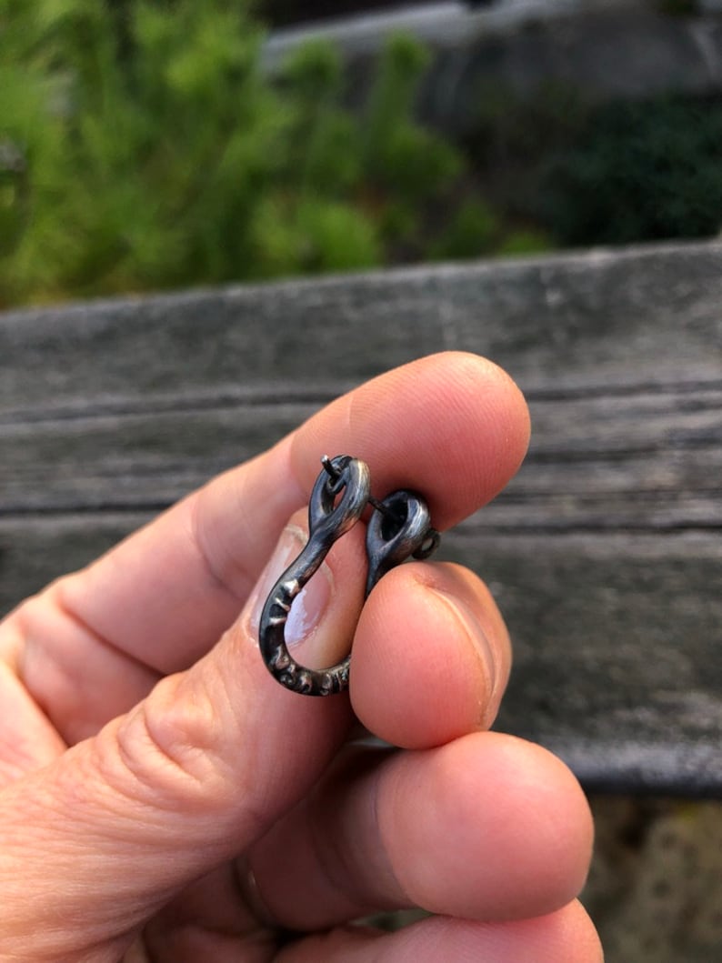 May include: A silver hoop earring with a textured finish. The earring is in the shape of a U and has a small loop at the top.