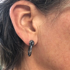 May include: A pair of black hoop earrings with a textured finish. The earrings are made of metal and have a simple, modern design.