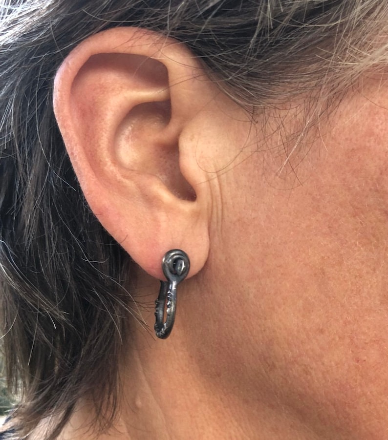 May include: A pair of black hoop earrings with a textured finish. The earrings are made of metal and have a simple, modern design.