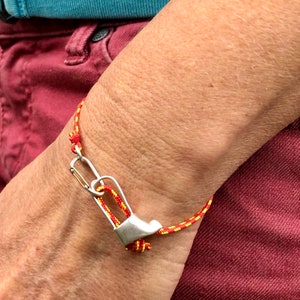 May include: A red and yellow braided bracelet with a silver carabiner clasp. The bracelet is worn on a person's wrist.