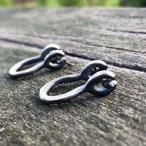 May include: A pair of silver hoop earrings with a unique twisted design. The earrings are made of metal and have a smooth, polished finish.