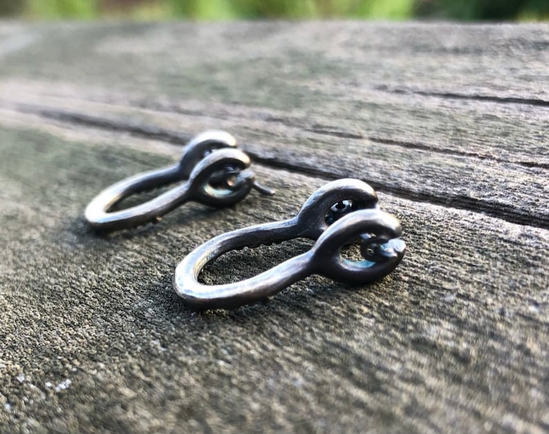 May include: A pair of silver hoop earrings with a unique twisted design. The earrings are made of metal and have a smooth, polished finish.