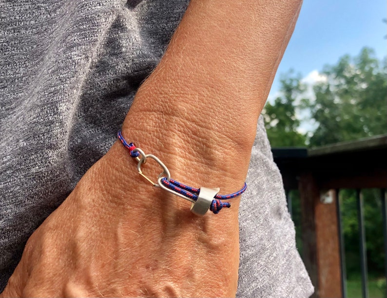 May include: A red and blue braided cord bracelet with a silver clasp and a silver oval charm.