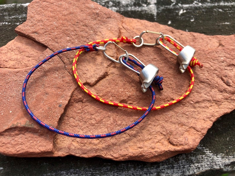 May include: Two bracelets made with red, yellow, and blue cord and silver metal clasps. The bracelets are tied together with a knot.