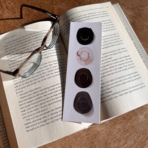 May include: A close-up of a bookmark with a watercolor illustration of three black cowboy hats. The bookmark is on top of an open book with the text "How to Stay Motivated in Life and Work" visible.