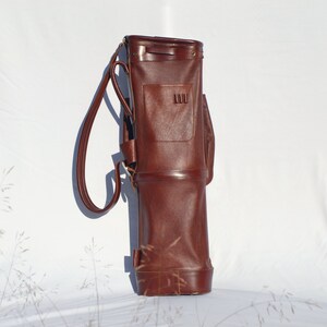 May include: A brown leather golf bag with a single strap and a small pocket on the front.