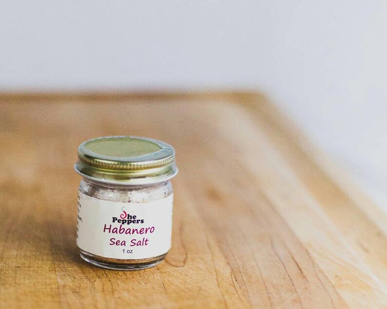 May include: A small glass jar with a gold lid filled with white sea salt. The label reads "The Peppers Habanero Sea Salt 1 oz."