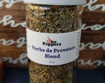 May include: A glass jar filled with dried herbs labeled "She Peppers Herbs de Provence Blend" with a white label and a white lid. The jar contains 2 ounces of herbs.