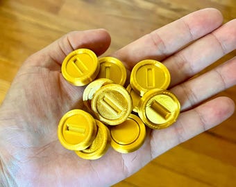 Op de afbeelding: Een hand die een stapel van acht gouden plastic munten vasthoudt met een enkele verhoogde lijn op elke munt.