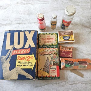 May include: A collection of vintage items, including a box of Lux Flakes, a box of Carnival Straws, and several small bottles and boxes. The Lux box features a woman in a dress. Other items include toothpicks and spoons.