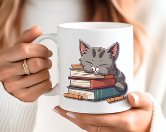 May include: White ceramic mug with a cartoon illustration of a gray cat sleeping on a stack of books. The cat has closed eyes and a pink nose.