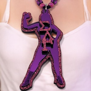 May include: A purple and glittery pendant necklace featuring a stylized figure with Greek letters. The pendant hangs from a black cord with purple beads. The figure is flexing its arm. The necklace is a statement piece.