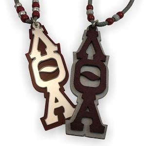 May include: Two silver and maroon necklaces with the letters "AOA" on the pendants. The necklaces are made of grey cord with red and white beads.