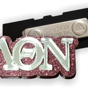 May include: A pink glitter magnetic pin with the letters "AON" in silver glitter. The pin has a black backing with a silver "Caution Magnetic" label.
