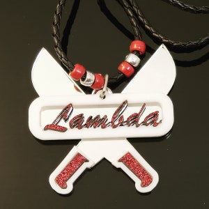 May include: A white necklace with a red glitter 'Lambada' pendant. The pendant is shaped like two crossed baseball bats.