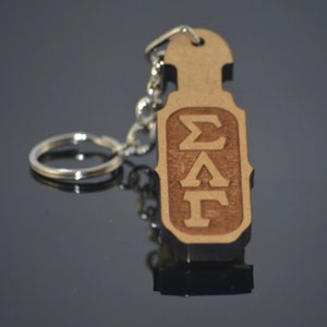 May include: A wooden keychain with a silver key ring. The keychain is shaped like a paddle and has the letters "ΣΑΓ" engraved on it.
