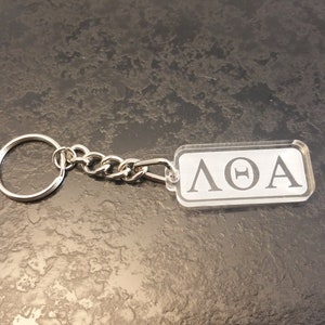 May include: A silver keychain with a clear rectangular tag that says "ΛΘΑ" in white lettering.