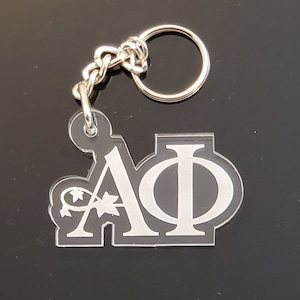 May include: A white acrylic keychain with the letters "AΦ" in a stylized font. The keychain has a silver chain attached to it.