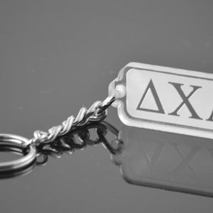 Peut inclure: Un porte-clés argenté avec un charme rectangulaire en acrylique orné des lettres "ΔΧΛ" en noir.