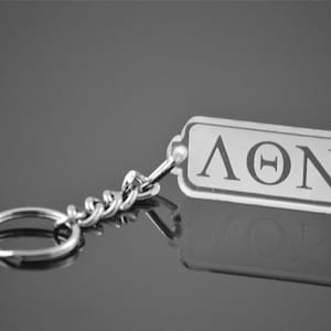 May include: A silver keychain with a clear acrylic charm that says "ΛΘΝ" in white lettering.