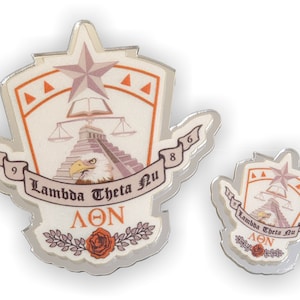 May include: Two silver pins with a white background and orange accents. The larger pin features a star, a book, a scale, a pyramid, an eagle, and the text "Lambda Theta Nu" and "ΛΘΝ". The smaller pin is a smaller version of the larger pin.