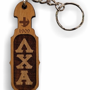 May include: A wooden keychain with a brown and black engraved design. The keychain features the letters "AXA" and the year "1909".