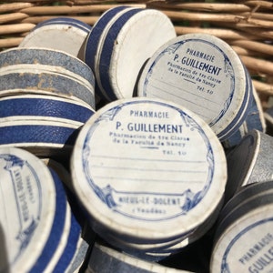 May include: A wicker basket filled with vintage round tin containers with blue and white labels. The labels read "Pharmacie P. Guillemment Pharmacien de tre Classe de la Faculte de Nancy Tel. 10".