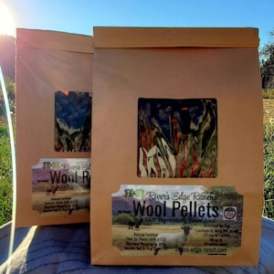 May include: Two brown paper bags with a window showing wool pellets inside. The bags have labels that say "River's Edge Ranch Wool Pellets 100% Regeneratively Raised Wool". The labels also include information about the product, such as its use as a natural fertiliser and its ability to decrease watering by 25%.