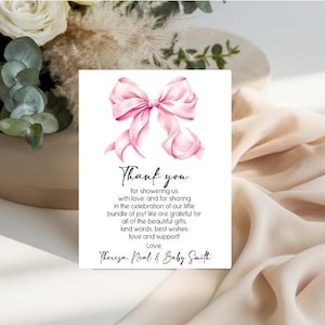 May include: A rectangular white thank you card featuring a large pink watercolor bow at the top. The text reads: Thank you for showering us with love, and for sharing in the celebration of our little bundle of joy! Love, Theresa, Neal & Baby Smith.