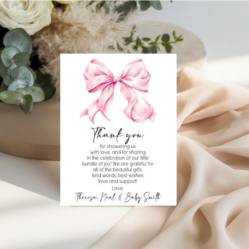 May include: A rectangular white thank you card featuring a large pink watercolor bow at the top. The text reads: Thank you for showering us with love, and for sharing in the celebration of our little bundle of joy! Love, Theresa, Neal & Baby Smith.
