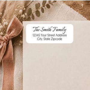 May include: A rectangular white address label with rounded corners featuring black text that reads The Smith Family, 12345 Your Street Address, City, State Zipcode. The label is placed on a light-colored envelope next to a dusty pink velvet ribbon.
