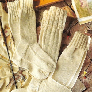 Könnte beinhalten: Drei Paar cremefarbene Stricksocken. Die Socken sind aus einem weichen, warmen Garn gefertigt und haben eine gerippte Struktur. Die Socken sind gefaltet und auf einer braunen Oberfläche angeordnet.