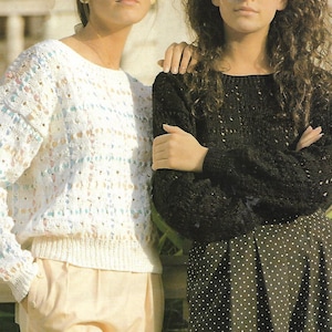 May include: Two women wearing sweaters. The woman on the left is wearing a white sweater with a colorful pattern. The woman on the right is wearing a black sweater with a small white polka dot pattern.