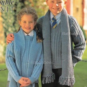 Puede incluir: Dos niños con conjuntos de punto a juego. La niña lleva un jersey y bufanda azul claro con flecos, y el niño un jersey y bufanda grises con flecos. Ambos llevan uniforme escolar. El texto "double knit" es visible.