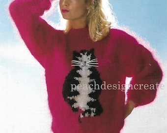 May include: A pink fuzzy sweater with a black and white cat design on the front. The cat has green eyes and a white stripe on its nose.