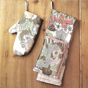 May include: A cream-coloured oven mitt and matching kitchen towel set. The floral pattern includes cherries, flowers, and leaves in shades of green, pink, and brown. The towel has a pink ribbon detail.