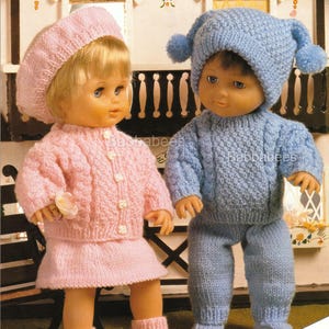 May include: Two dolls dressed in knitted outfits. One doll wears a pink beret, sweater, skirt, and booties. The other doll is in a blue knit hat with pom-poms, a sweater, and pants. The outfits are handmade and suitable for dolls and miniature babies.