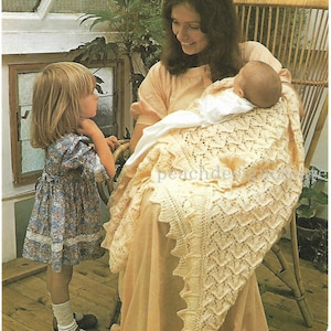 May include: A woman holding a baby wrapped in a crocheted cream-coloured blanket with a lacy pattern. A young girl in a floral dress stands nearby. The woman and baby are sitting in a wicker chair.