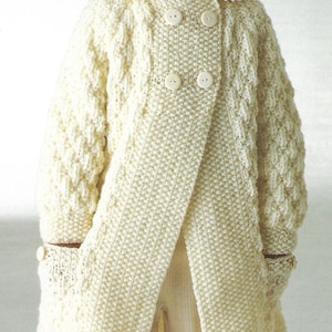 May include: A white knitted cardigan with a double breasted closure and pockets. The cardigan features a cable knit pattern and is made from a soft yarn.