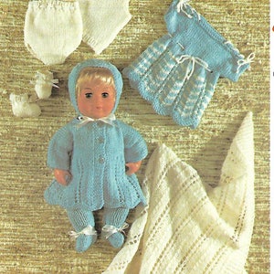 May include: A set of knitted doll clothes in blue and white. The set includes a dress, a coat, a hat, pants, booties, and a diaper. The clothes are laid out on a brown and white patterned surface.