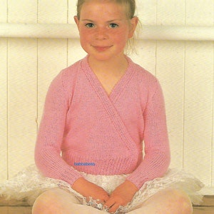 May include: A pink knitted wrap cardigan with a V-neck and long sleeves. The cardigan is worn over a white tulle skirt.